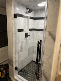 a shower with a glass door and black and white tile