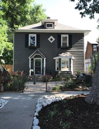 a gray house with black shutters and a tree in the front yard